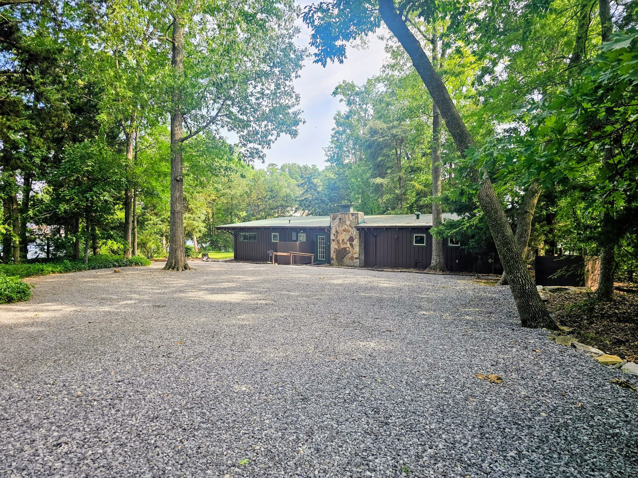 Gravel driveway and parking area with the cabin nestled among tall trees at Guntersville Getaway