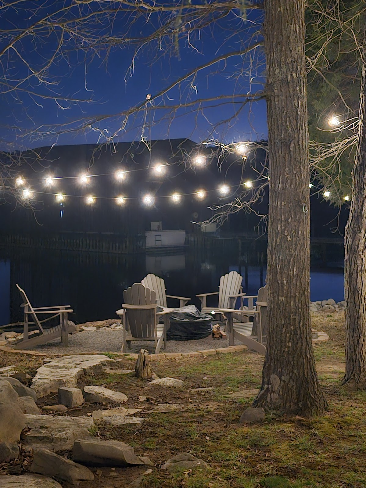 Adirondack chairs and covered fire pit under string lights with the boathouse glowing beyond at Guntersville Getaway