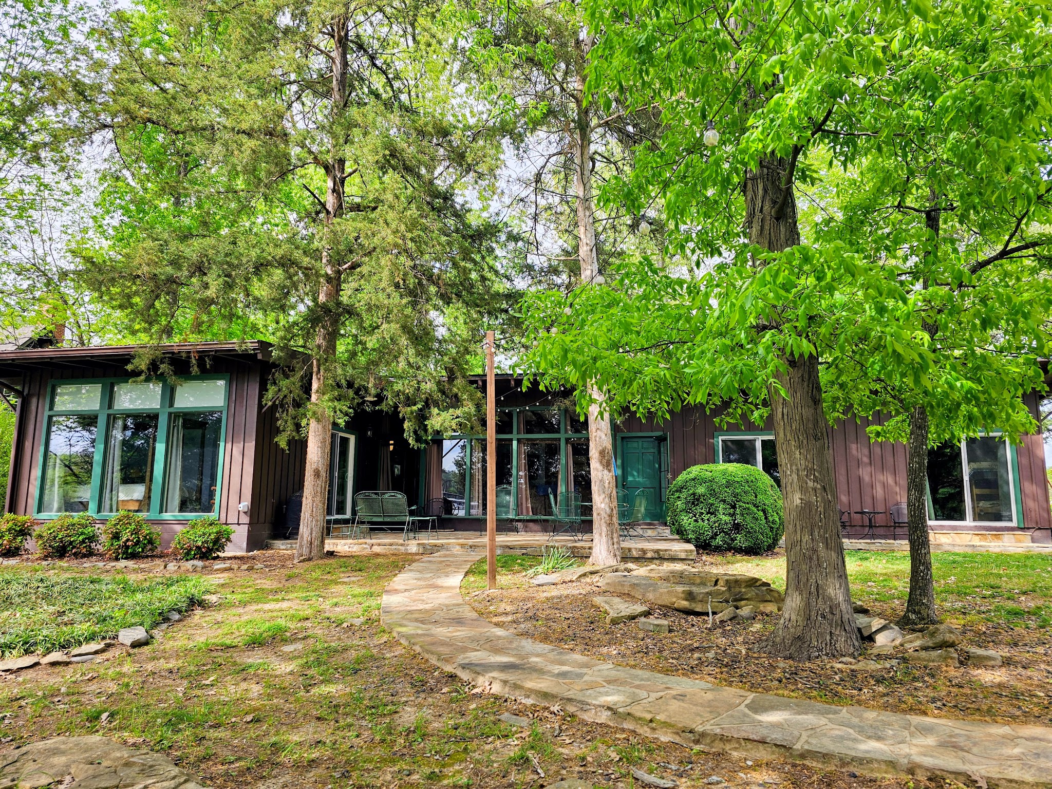 Front yard of Guntersville Getaway under a lush green tree canopy with stone walkway leading to the lakefront cabin