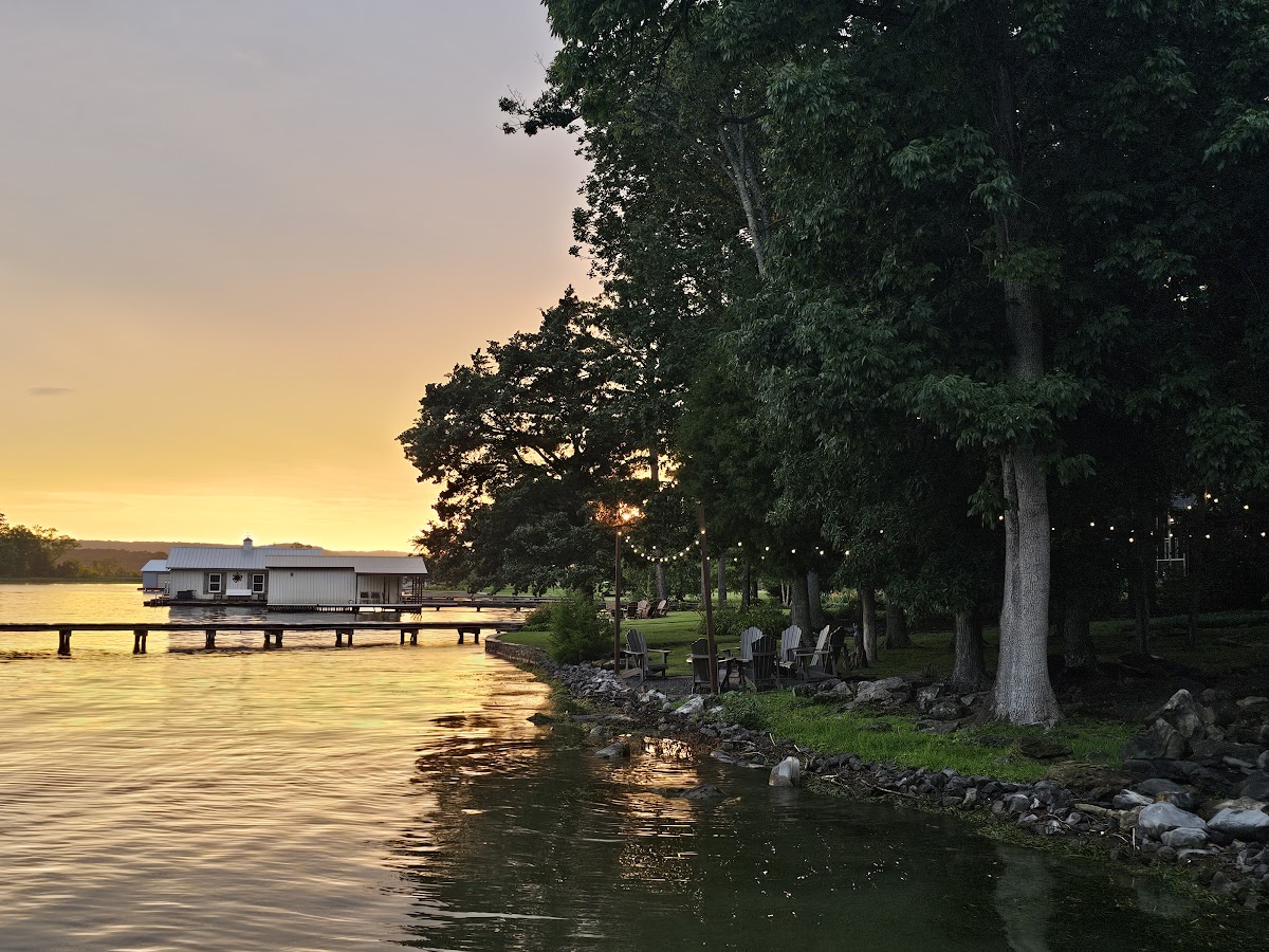 Golden summer sunset over the cove with boathouse, Adirondack chairs, and string lights at Guntersville Getaway